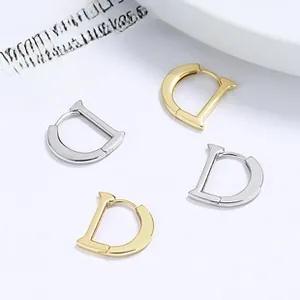 Detailed macro view of D-letter shaped hoop earrings in polished gold and silver finishes