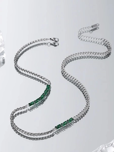 Macro detail of silver necklace with green emerald-cut zircon stones and twisted chain