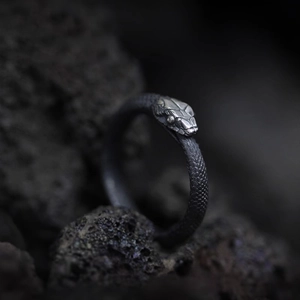 Macro shot of silver snake ring with textured scales on dark volcanic rock