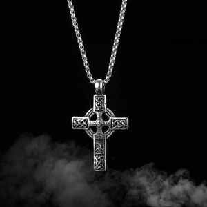 Détail du collier croix celtique argentée avec motifs de nœuds sur fond sombre et fumé