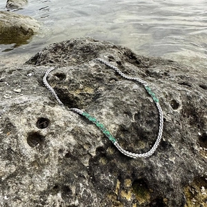 Silver woven necklace with emerald zircon accents on a natural rock background