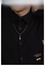 Détail d'un collier avec pendentif géométrique argenté sur un homme en chemise noire