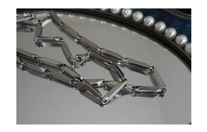 Detail of silver rhombus titanium steel chain with lobster clasp on reflective mirror surface