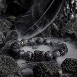 Handmade volcanic stone beaded bracelet with gold accents on a misty black rock backdrop