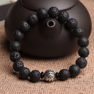 Macro view of volcanic stone beads with a vintage silver dragon metal charm on a bracelet