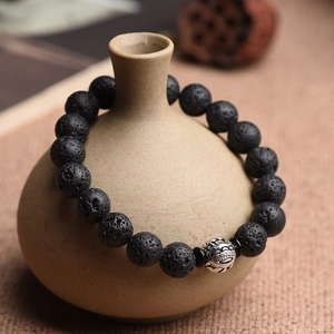 Detail of volcanic stone beads and silver-tone charm on an elastic bead bracelet