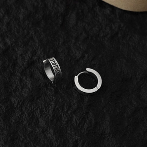 Close-up of silver punk rune clip-on earrings on a dark textured rock background