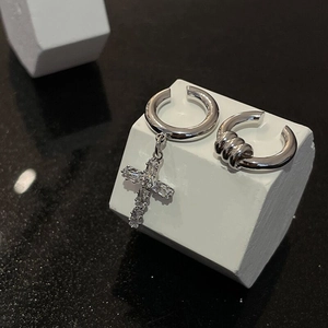 Close-up of silver ear cuffs with cross pendant and zircon on white geometric blocks