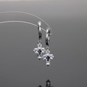 Silver stainless steel huggie earrings with zirconia cross pendants on a dark background