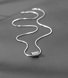 Macro shot of silver-toned snake chain necklace featuring a textured cylinder pendant