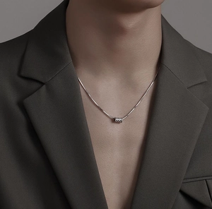 Close-up of a silver cylindrical pendant with textured weave pattern on a snake chain