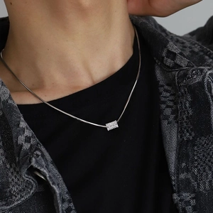 Men's silver snake chain necklace with textured cylindrical pendant on denim jacket