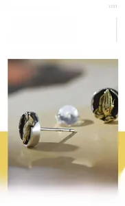 Macro shot of silver circular stud earrings with golden praying hands relief carving