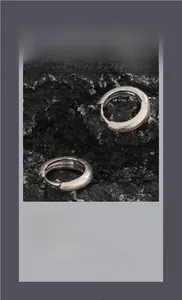 Détail de boucles d'oreilles créoles argentées texturées sur fond minéral sombre