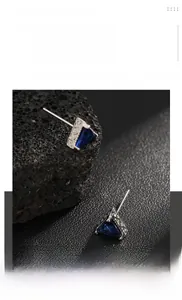 Macro shot of titanium steel triangle stud earrings with blue sapphire rhinestones on rock