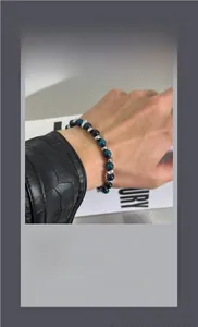 Blue tiger eye beads and irregular silver metal charms on a wrist with a black jacket