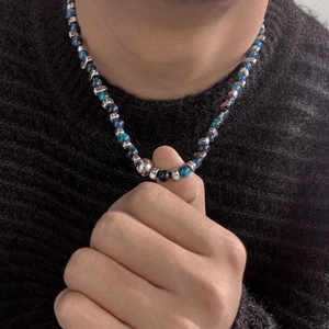 Collier de perles bleues avec intercalaires argentés porté sur un pull noir pour homme