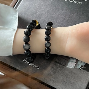 Bracelets en perles d'obsidienne avec charmes dorés portés par une personne