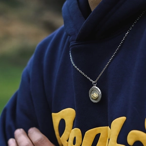 Collier en acier titane avec pendentif montagne dorée sur un fond extérieur naturel