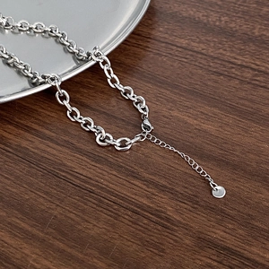 Minimalist silver cross necklace with adjustable chain and round tag on wooden surface