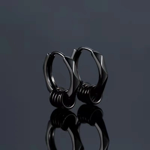 Détail de boucles d'oreilles noires géométriques avec trois anneaux sur fond sombre