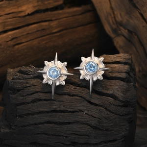 Star-shaped silver earrings with blue sapphire centerpiece on a rustic wooden background