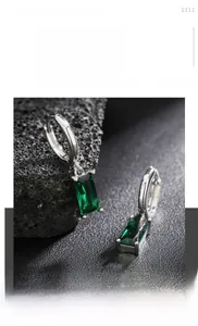 Macro view of titanium steel earrings with emerald green gemstones on volcanic rock