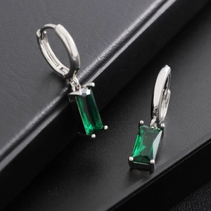 Silver huggie earrings with rectangular emerald green stones shown on a leather display