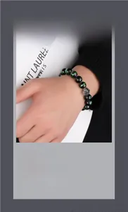 Detailed close-up of dark green beaded bracelet with a silver geometric metal charm