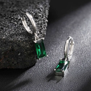 Elegant emerald green rectangular stone earrings with silver hoop on black volcanic rock