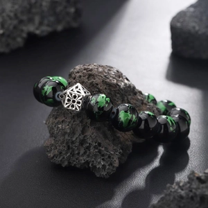 Green Seraphinite beaded bracelet with silver filigree bead on dark volcanic rock background