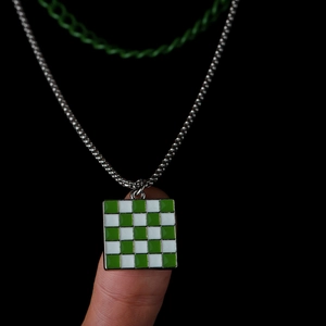 Green and white checkerboard square pendant necklace with silver chain on a hand