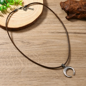 Collier vintage avec pendentif croissant tribal et cordon tressé marron sur fond de bois