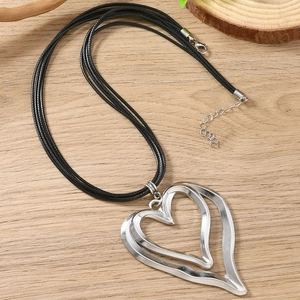 Double-layered silver heart pendant necklace with black cord on a wooden surface