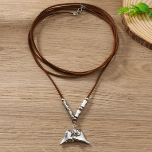 Detail of silver heart pendant with brown woven cord on minimalist wooden surface