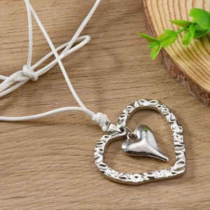 Collier double cœur martelé en argent avec cordon blanc sur une surface en bois naturel