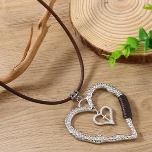 Collier en cuir vintage avec pendentifs double cœur et croix sur fond en bois naturel