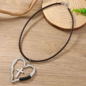 Détail du pendentif cœur et croix vintage sur cordon cuir marron sur fond en bois rustique