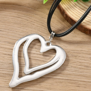Close-up of a double-layer hollow heart pendant on a black cord over wood texture