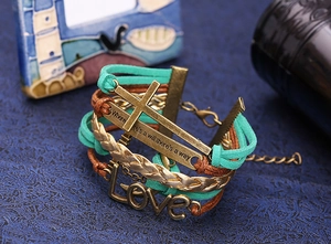 Dettaglio del bracciale multistrato con croce, ciondolo love e barra con citazione incisa