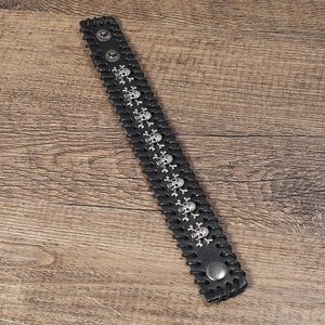 Detail of black woven leather punk bracelet featuring vintage silver skull row on wood