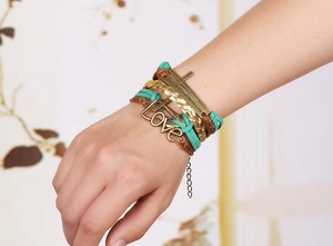 Dettaglio macro del bracciale intrecciato multistrato con ciondolo LOVE e piastra