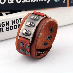 Punk style wide leather bracelet with metal skulls and rivets on a vintage book background