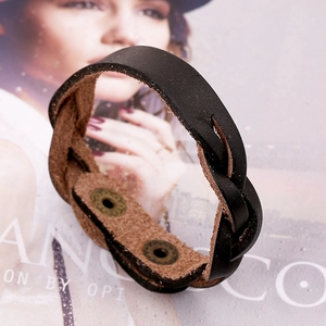 Bracelet rétro en cuir tressé noir avec boutons pressions en métal sur fond de magazine de mode