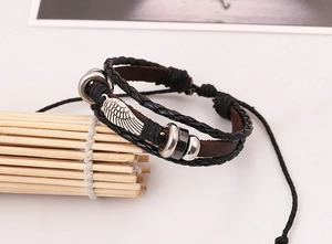 Macro view of multi-layer leather bracelet featuring an intricate silver wing pendant