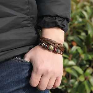 Brown lychee grain leather bracelet with vintage metal disc worn on wrist in outdoor setting