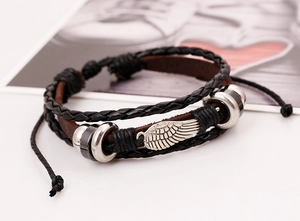 Macro detail of multi-layer leather bracelet with silver wing charm and braided texture