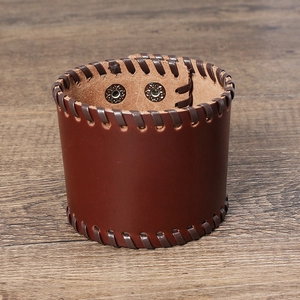 Detailed view of dark brown leather wide wristband with woven edges and metal snap buttons