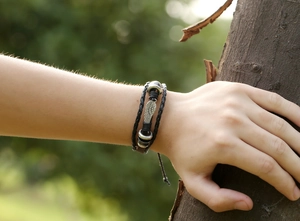 Close-up of adjustable punk style braided leather bracelet with silver wing pendant on arm
