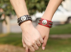 Gros plan de bracelets punk en cuir avec clous tête de mort portés par un couple